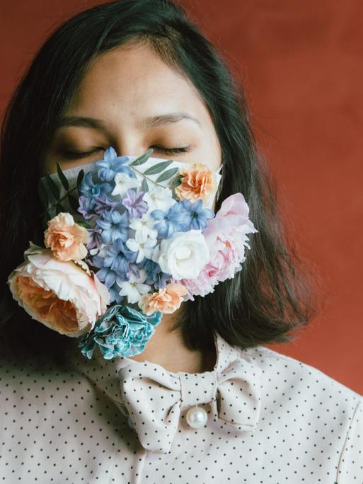 Eine Frau trägt eine Atemschutzmaske, die über und über mit Blüten bedeckt ist.