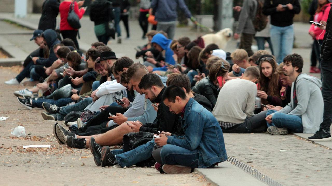 Im Berliner Lustgarten sitzen junge Menschen auf dem Boden und starren auf die Displays ihrer Smartphones.