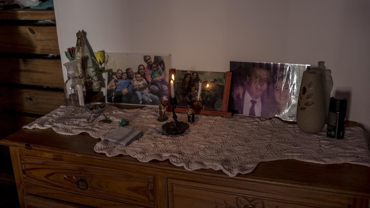 Auf einer Kommode stehen auf einem weißen Deckchen vor einer brennenden Kerze mehrere gerahmte Fotos, die u.a. den Vater mit der Tochter zeigen.