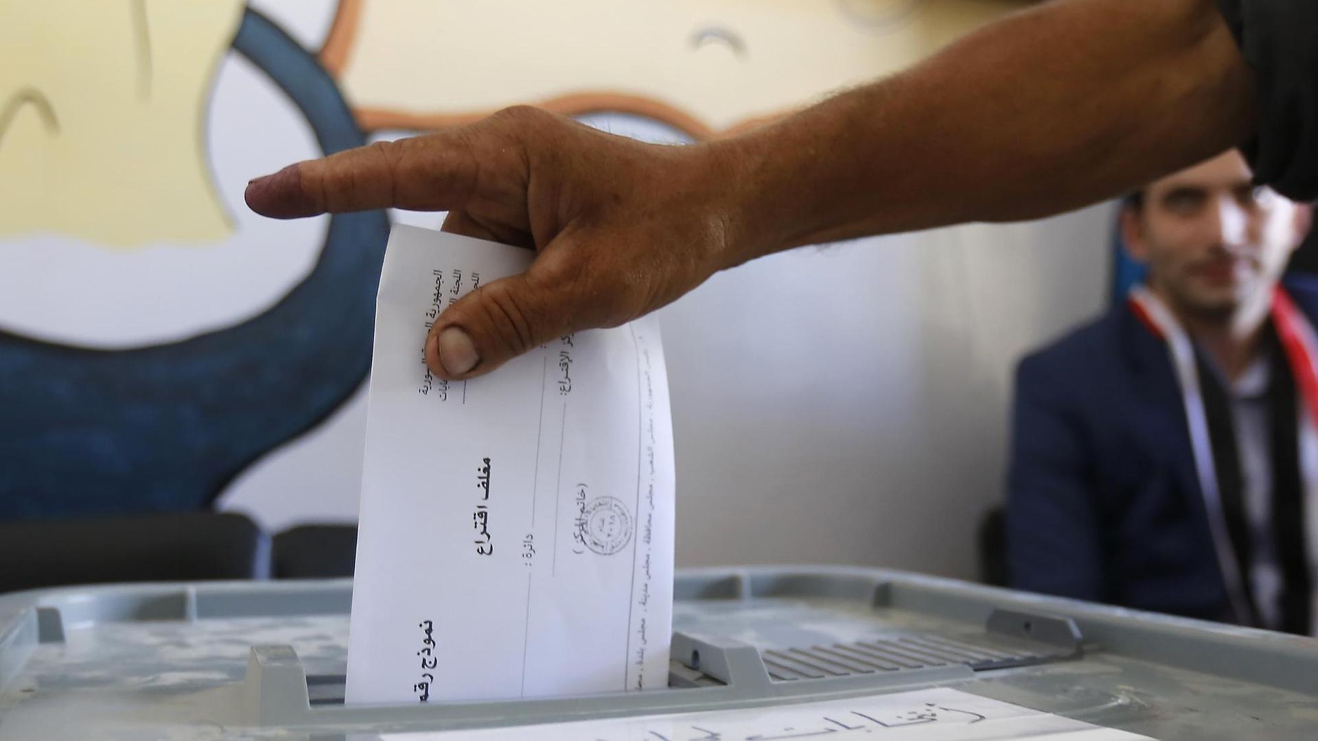 Man sieht die Hand eines Mannes, der einen Wahlzettel in eine Wahlurne wirft.