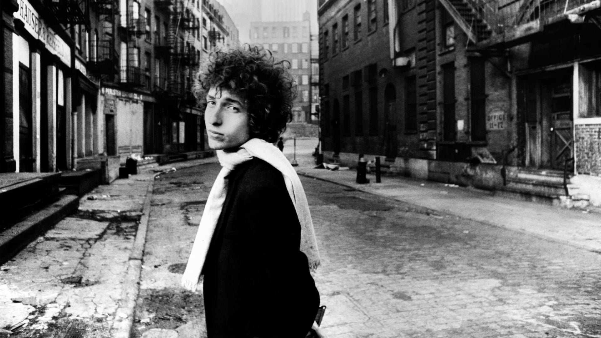 Das Schwarz-weiß-Foto zeigt Bob Dylan mit Wuschelfrisur und weißem Schal in einer leeren Straße in New York 1966