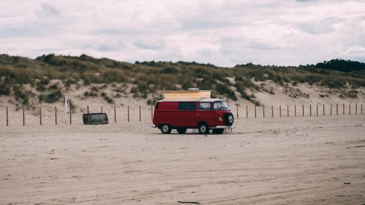 Ein roter Camper steht alleine an einem Strand.
