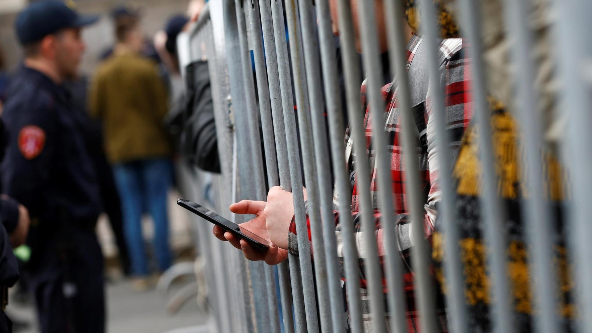 Ein Demonstrant in Moskau bedient sein Smartphone hinter einem Gitterzaun.