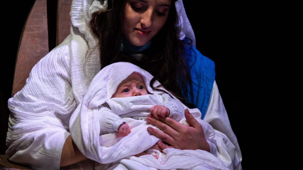 Eine Maria Darstellerin in einem biblischem Kostüm mit echtem Baby auf dem Schoß in einem Krippenspiel.