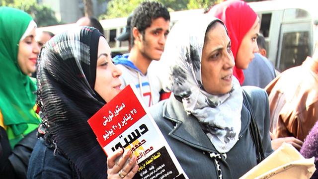 Zwei Frauen mit Kopftuch in Ägypten halten den Entwurf der neuen Verfassung in der Hand. Im Hintergrund sind noch andere Frauen und Männer zu sehen.