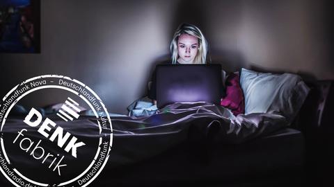 Eine Frau sitzt im Dunkeln in ihrem Bett und schaut auf ihren Laptop. (Mit Denkfabrik-Stempel)