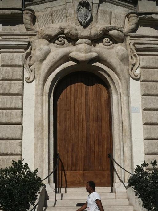Ein Passant geht am Palazzo Zuccari vorbei, dessen Eingangstür und Fenster wie Münder von Gesichtern geformt sind.