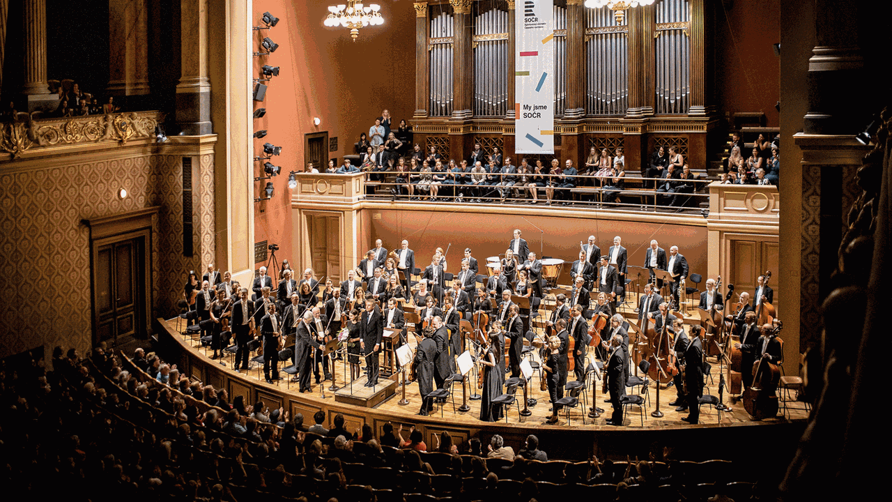 Auf der Bühne eines historischen Saales, unter einer großen Orgel, steht das Orchester und nimmt Beifall entgegen.