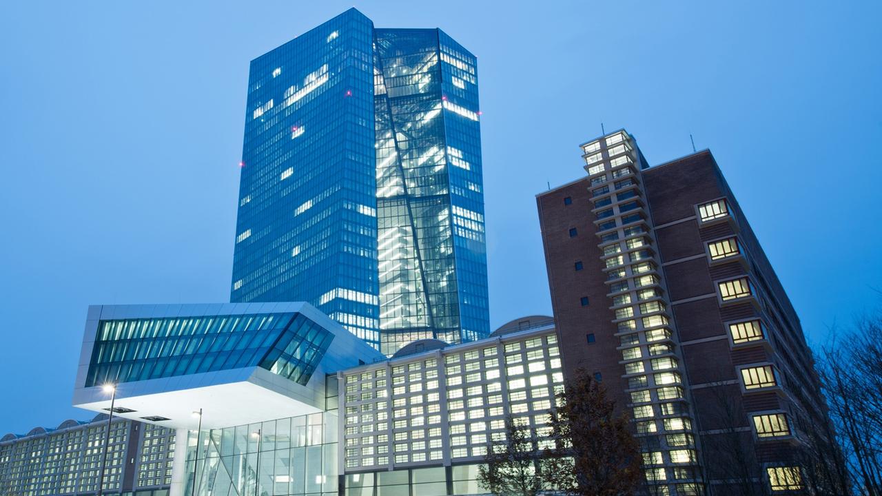 Außenansicht des EZB-Neubaus in Frankfurt in der Abenddämmerung. Hinter einem langgestreckten Gebäude erhebt sich ein gewundener Turm.