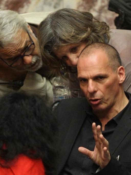Der griechische Finanzminister Yanis Varoufakis sitzt gestikulierend auf einem Stuhl im Parlament in Athen, er ist umringt von Parlamentsmitgliedern.