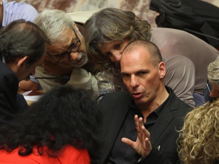 Der griechische Finanzminister Yanis Varoufakis sitzt gestikulierend auf einem Stuhl im Parlament in Athen, er ist umringt von Parlamentsmitgliedern.