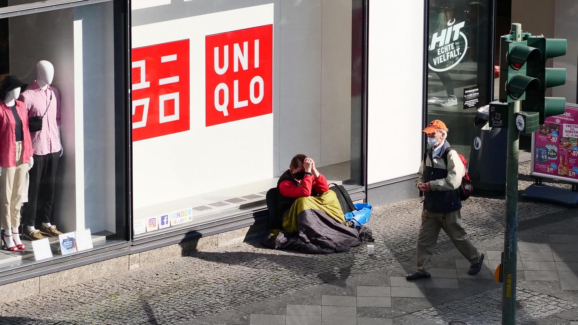 16.05.2020, Berlin. Ein Obdachloser sitzt an einer Einkaufsstrasse in Steglitz vor einem Laden und traegt einen Mundschutz. Ein älterer Mann mit Mundschutz geht an ihm vorbei.