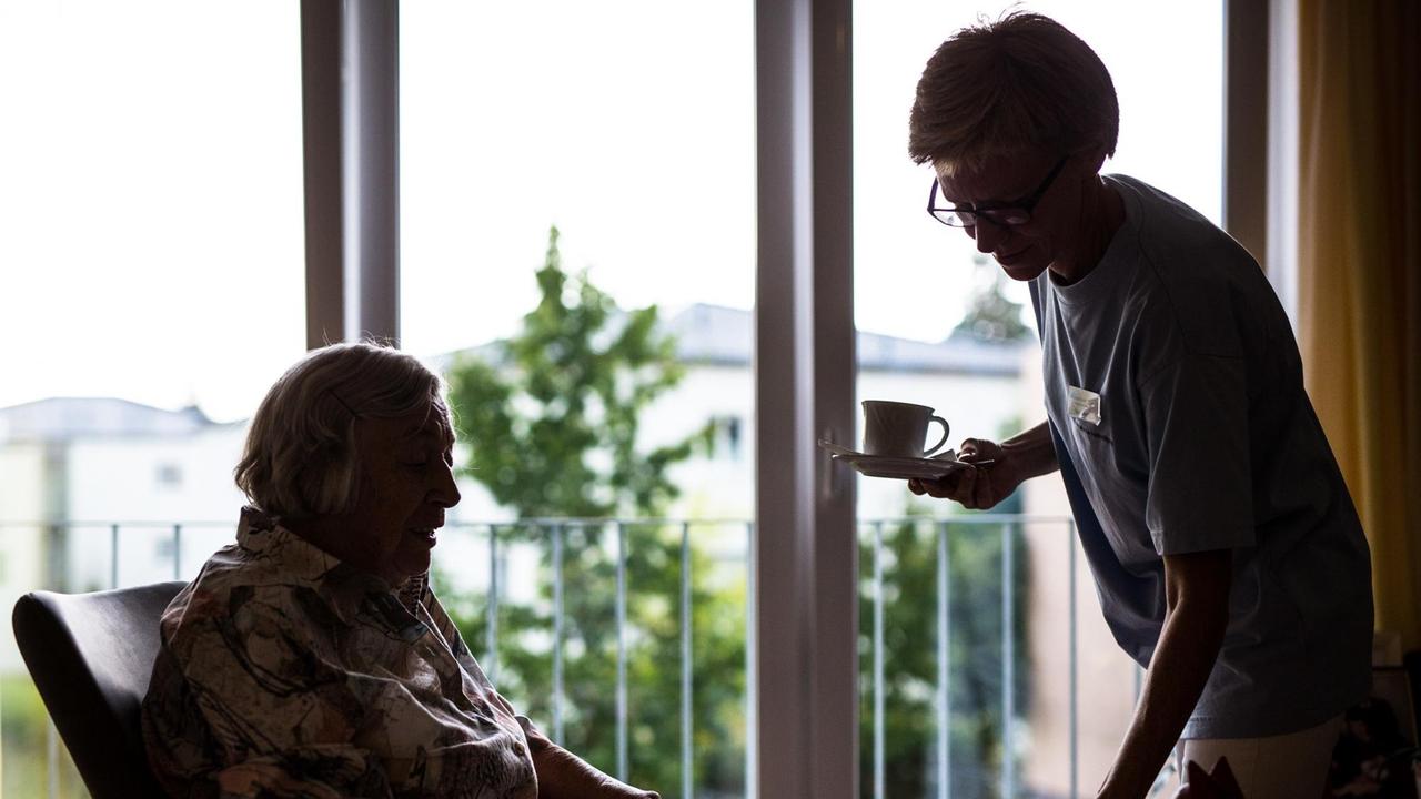 23.08.2018, Baden-Württemberg, Stuttgart: Eine Pflegekraft kümmert sich in einem Pflegeheim um eine ältere Dame und bringt ihr Kaffee und Kuchen. 