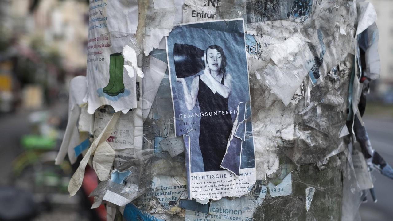 Anzeige für Gesangsunterricht an einem mit unzähligen Anzeigen überklebeten Laternenmast in Berlin-Prenzlauer Berg 