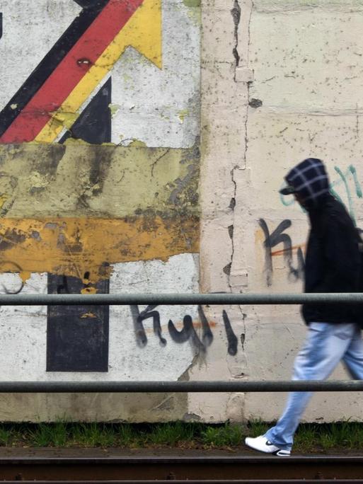 Ein Passant geht am 30.03.2012 an einer Schallschutzmauer in Magdeburg an einem aus der Wendezeit stammenden verwitterten Wandbild mit dem Schriftzug «Gemeinschaftswerk Aufschwung Ost» vorbei.