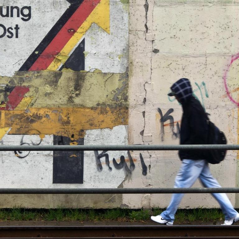 Ein Passant geht am 30.03.2012 an einer Schallschutzmauer in Magdeburg an einem aus der Wendezeit stammenden verwitterten Wandbild mit dem Schriftzug «Gemeinschaftswerk Aufschwung Ost» vorbei. 