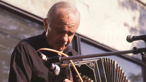 Ein Mann sitzt mit seinem Bandoneon vor einem Mikrofon und spielt vertieft.