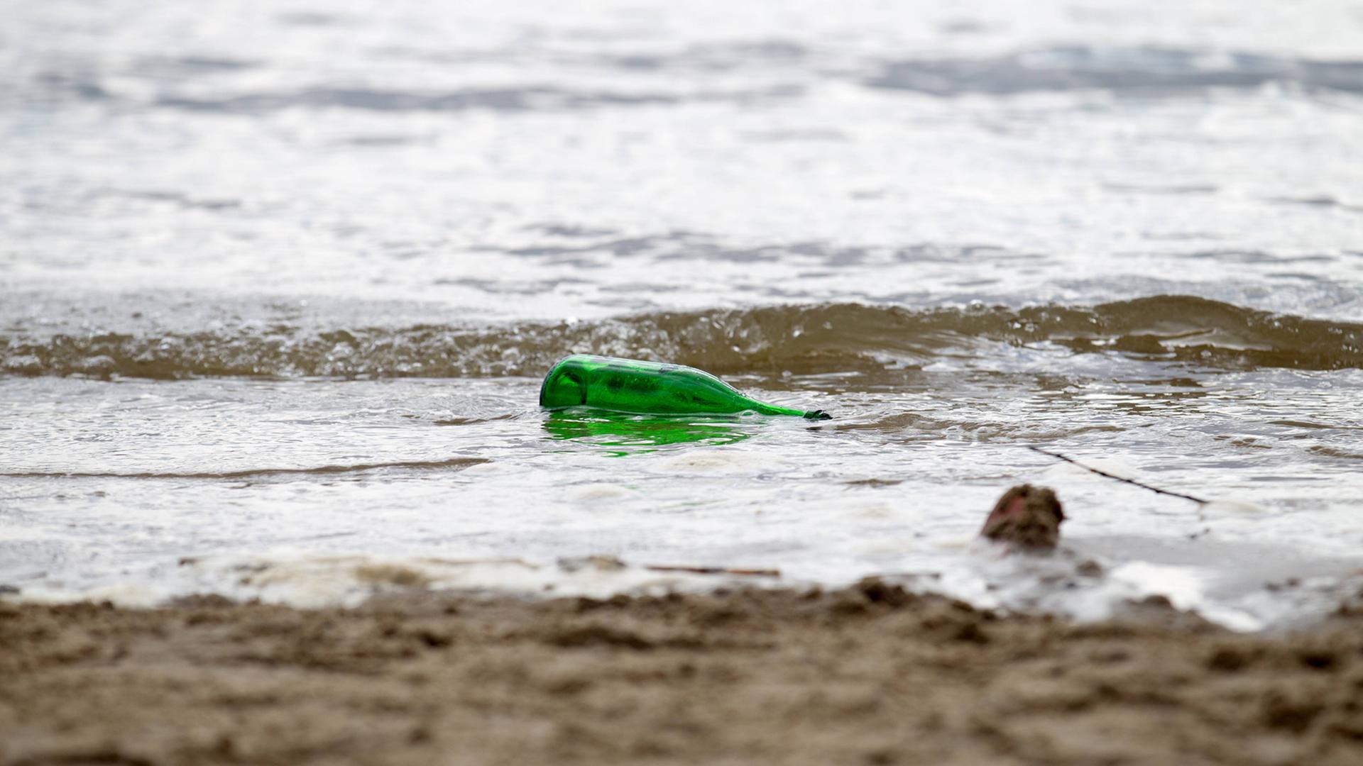 Eine Flasche mit Flaschenpost liegt in der Meeresbrandung an einem Strand.