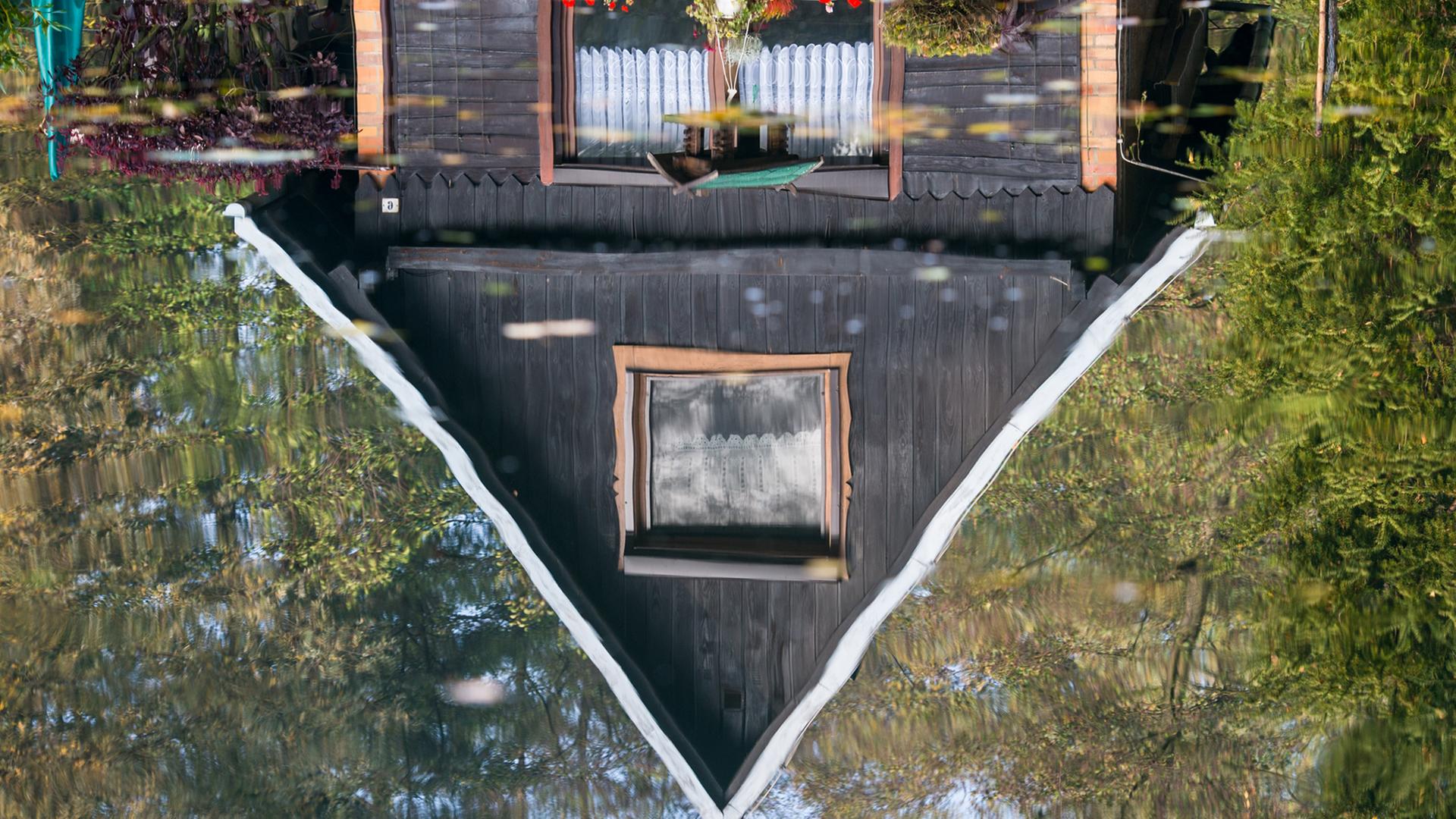Ein Holzhaus spiegelt sich im Wasser eines Fließes im Spreewaldort Lübbenau (Brandenburg).