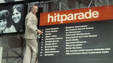 Moderator Dieter Thomas Heck steht auf einer Leiter vor dem Chart der Hitparade im Jahr 1974