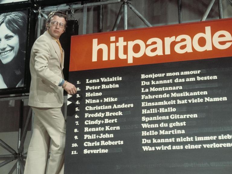 Moderator Dieter Thomas Heck steht auf einer Leiter vor dem Chart der Hitparade im Jahr 1974