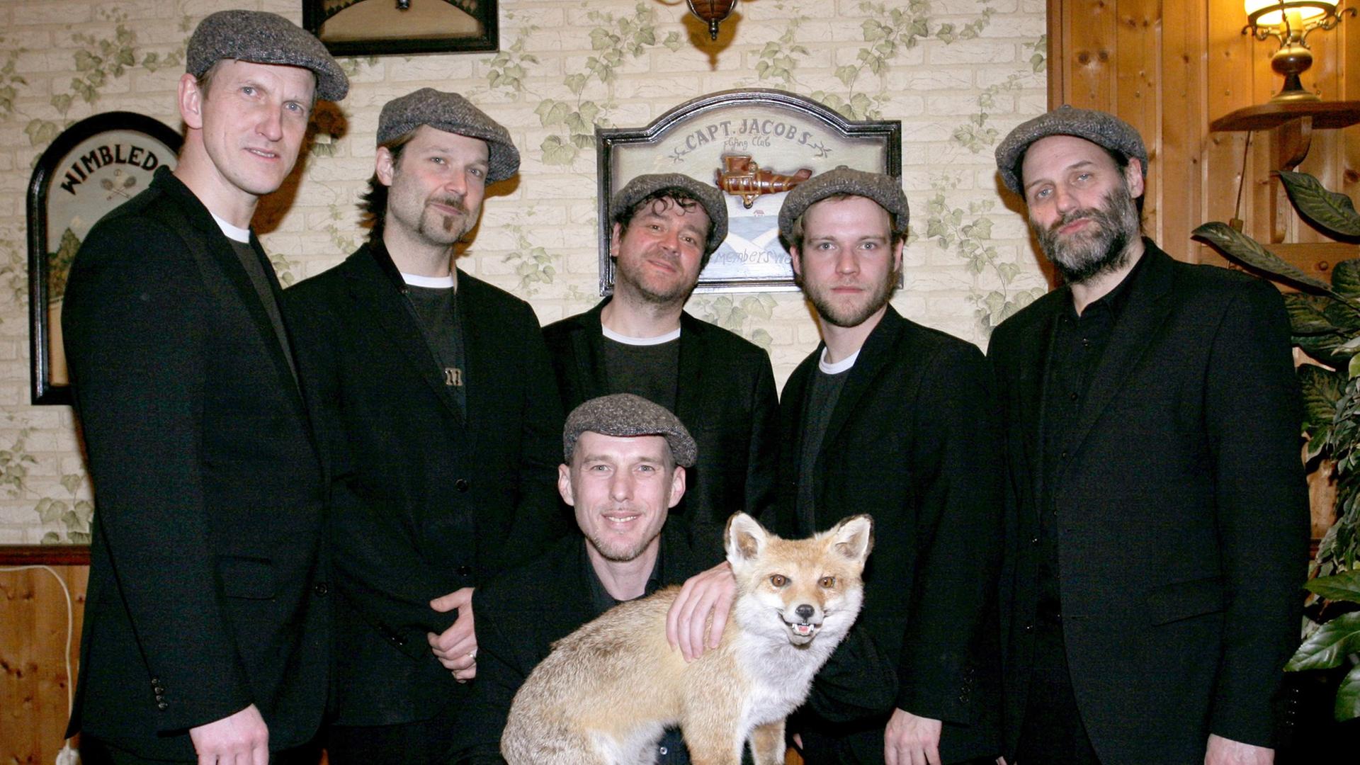 Die Mitglieder der Band "Jazzkantine" stehen zusammen in schwarzen Anzügen. Einer kniet in der Mitte und hält einen ausgestopften Fuchs in den Händen.