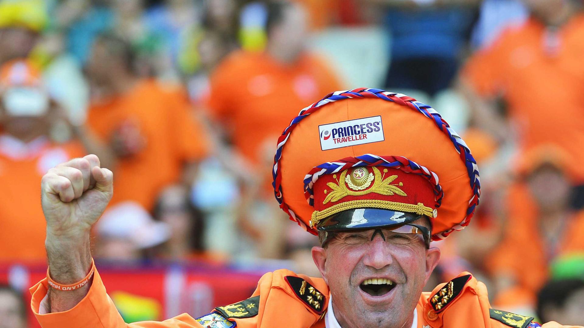 Niederländischer Fußballfan bei der Fußball-WM in Brasilien - mit orangener Mütze und Jacket und einer Fliege in den Farben der niederländischen Flagge. Er ballt siegesgewiss eine Faust.