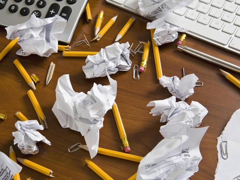 Zerknülltes Papier und abgebrochene Bleistifte auf einem Schreibtisch.