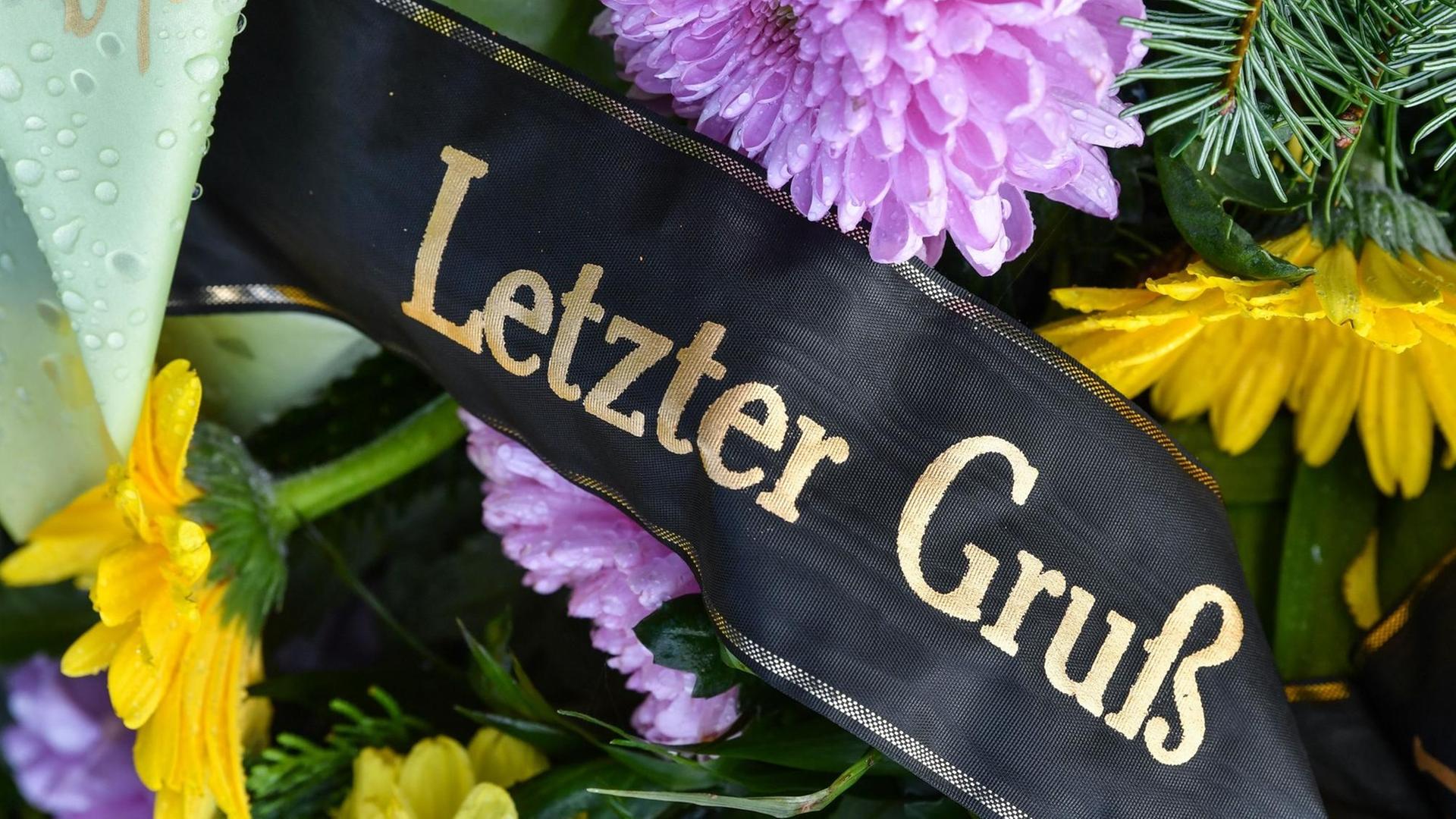 Eine Trauerschleife mit der Aufschrift "Letzter Gruß" auf einem Grab ist zu sehen