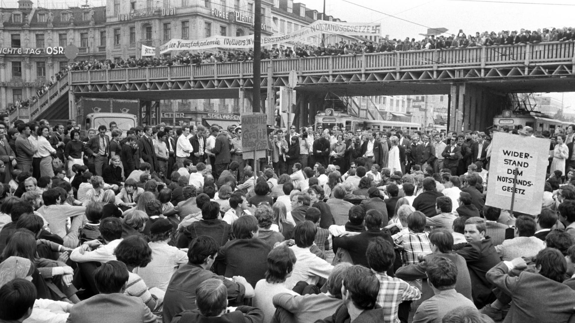 Dichtgedrängt stehen Demonstranten auf der Fußgänger-Notbrücke über dem Münchner Stachus; die Straßenbahnen wurden von den sitzenden Demonstranten blockiert. Am 29.05.1968, dem Vortag der dritten Lesung der Notstandsgesetze im Bonner Bundestag, demonstrierten in München tausende Studenten, Schüler, Arbeiter und Angestellte.