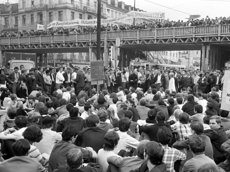 Dichtgedrängt stehen Demonstranten auf der Fußgänger-Notbrücke über dem Münchner Stachus; die Straßenbahnen wurden von den sitzenden Demonstranten blockiert. Am 29.05.1968, dem Vortag der dritten Lesung der Notstandsgesetze im Bonner Bundestag, demonstrierten in München tausende Studenten, Schüler, Arbeiter und Angestellte.