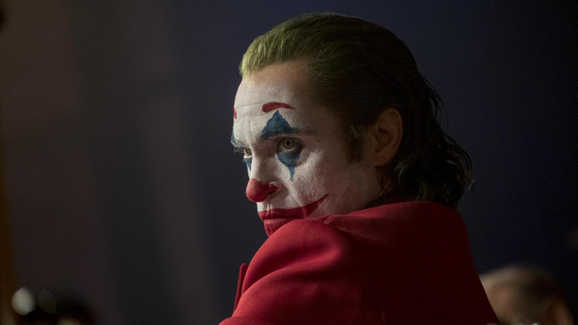 Joaquin Phoenix schaut über die linke Schulter, mit Clownsschminke im Gesicht und grünen Haaren.