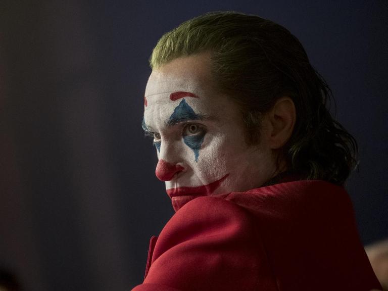Joaquin Phoenix schaut über die linke Schulter, mit Clownsschminke im Gesicht und grünen Haaren.
