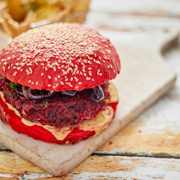 Veganer rot eingefärbter Burger von oben auf einem Holzbrett liegend fotografiert