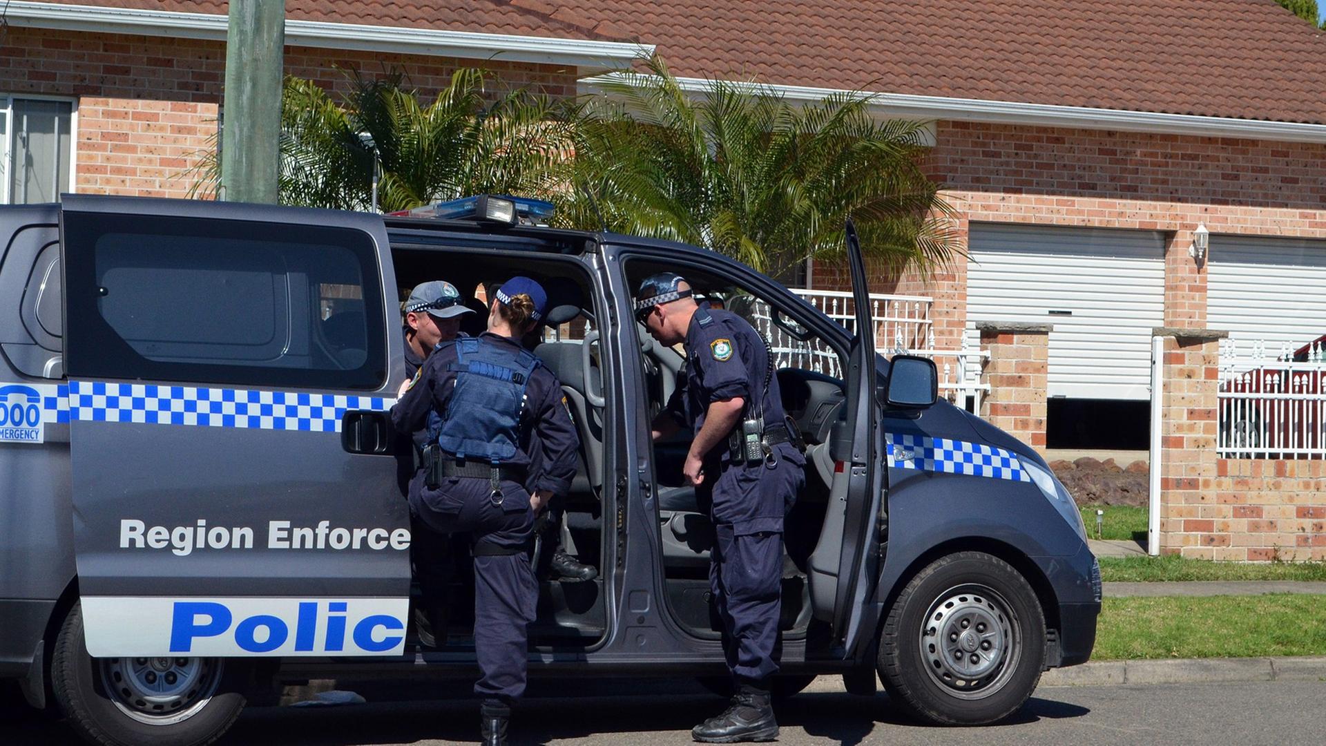 Australische Polizisten steigen in einen Mannschaftswagen vor einem Wohnhaus.