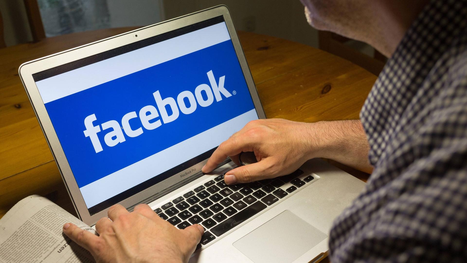 Computernutzer sitzt am Laptop mit dem Logo des sozialen Netzwerks Facebook
