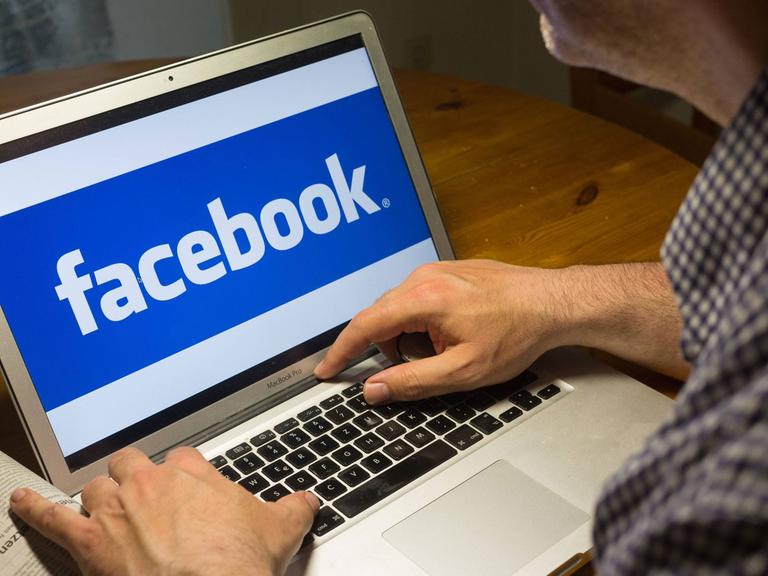 Computernutzer sitzt am Laptop mit dem Logo des sozialen Netzwerks Facebook