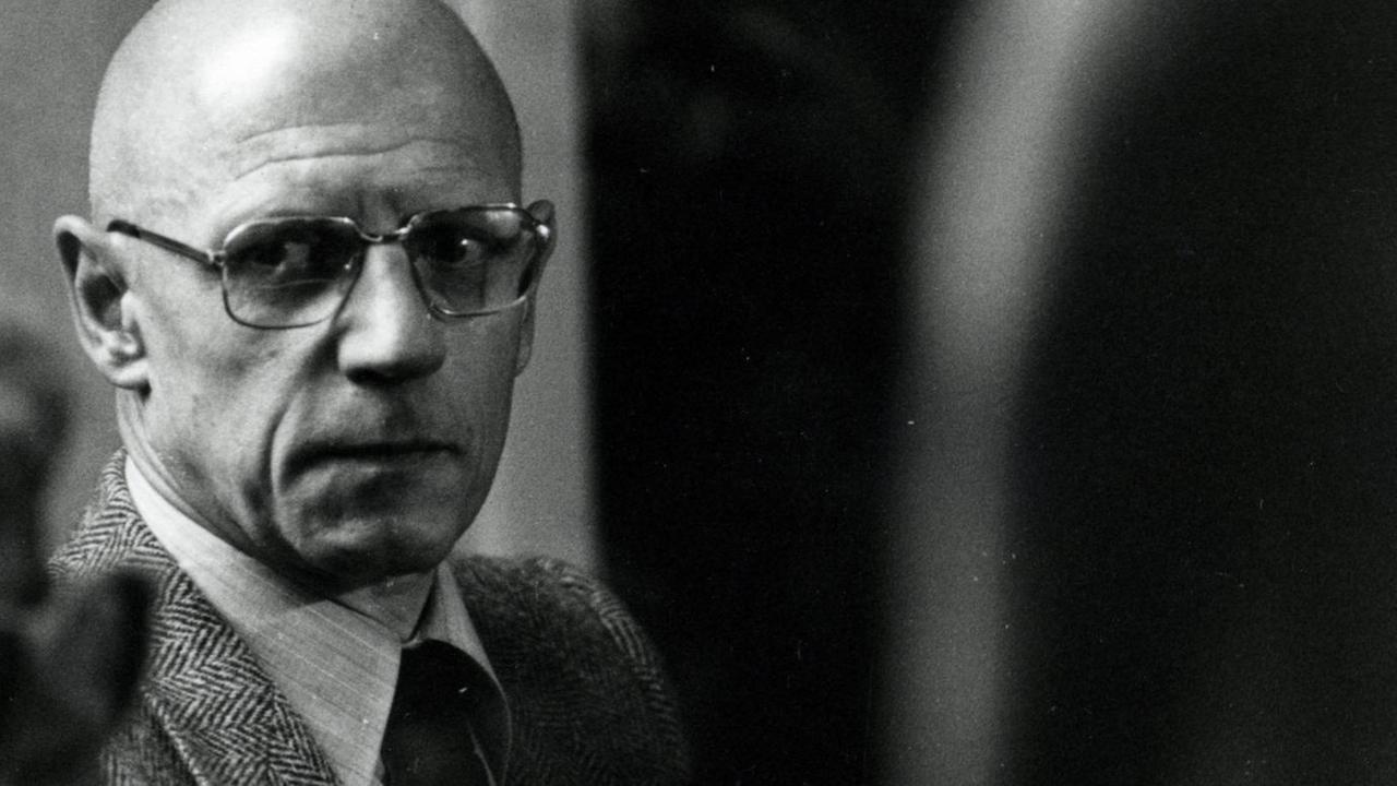 Der französische Philosoph Michel Foucault schaut aus den Augenwinkel an der Kamera vorbei. Er trägt eine große Brille.