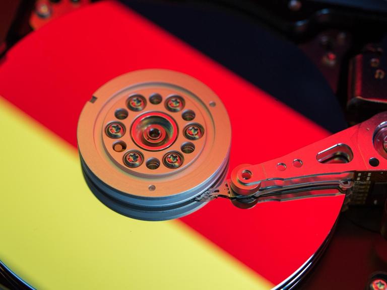 Die Farben einer Deutschlandfahne spiegeln sich in der Scheibe einer geöffneten Computerfestplatte