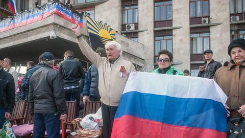 Prorussische Demonstranten in Donezk halten eine russische Fahne vor sich.