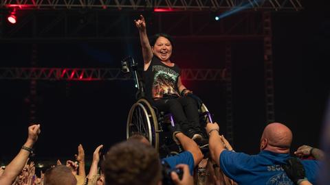 Wacken Open Air 2018, Frau im Rollstuhl steht am Bühnenrand vor begeistertem Publikum, im Hintergrund eine dunkle Bühne