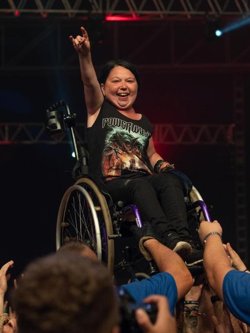 Wacken Open Air 2018, Frau im Rollstuhl steht am Bühnenrand vor begeistertem Publikum, im Hintergrund eine dunkle Bühne
