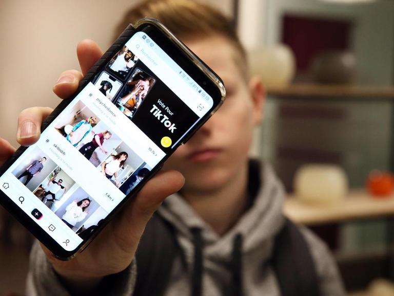 Ein Junge hält sein Smartphone in die Kamera, auf dem die App TikTok geöffnet ist