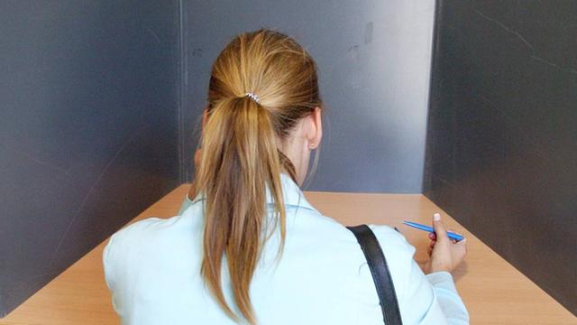 Eine Frau sitzt in der Wahl-Kabine mit dem Wahl-Zettel