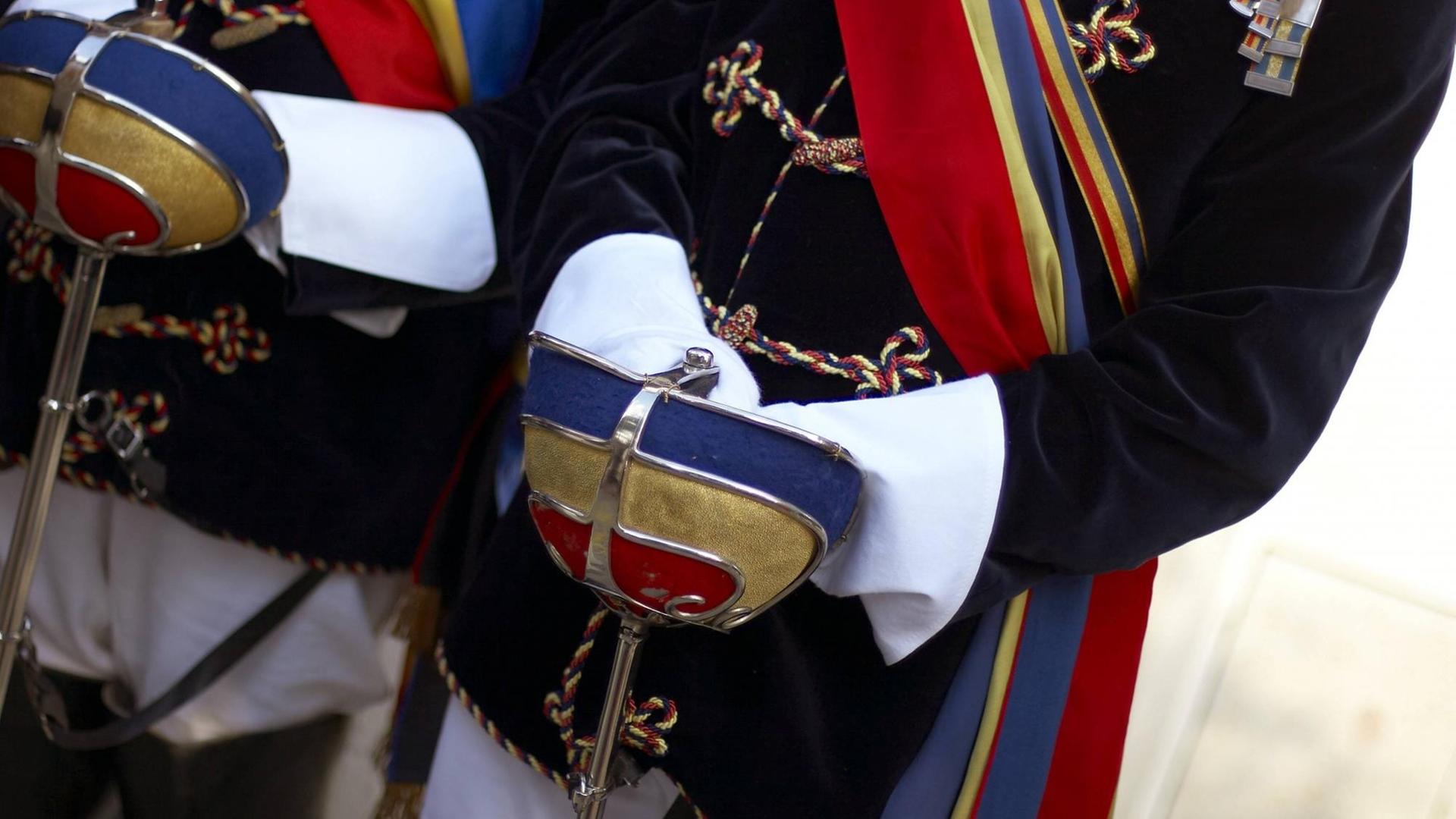 Degenglocken in den Burschenfarben Rot-Gold-Blau der Katholisch Österreichischen Hochschulverbindung Pannonia werden in weiß behandschuhten Händen gehalten.