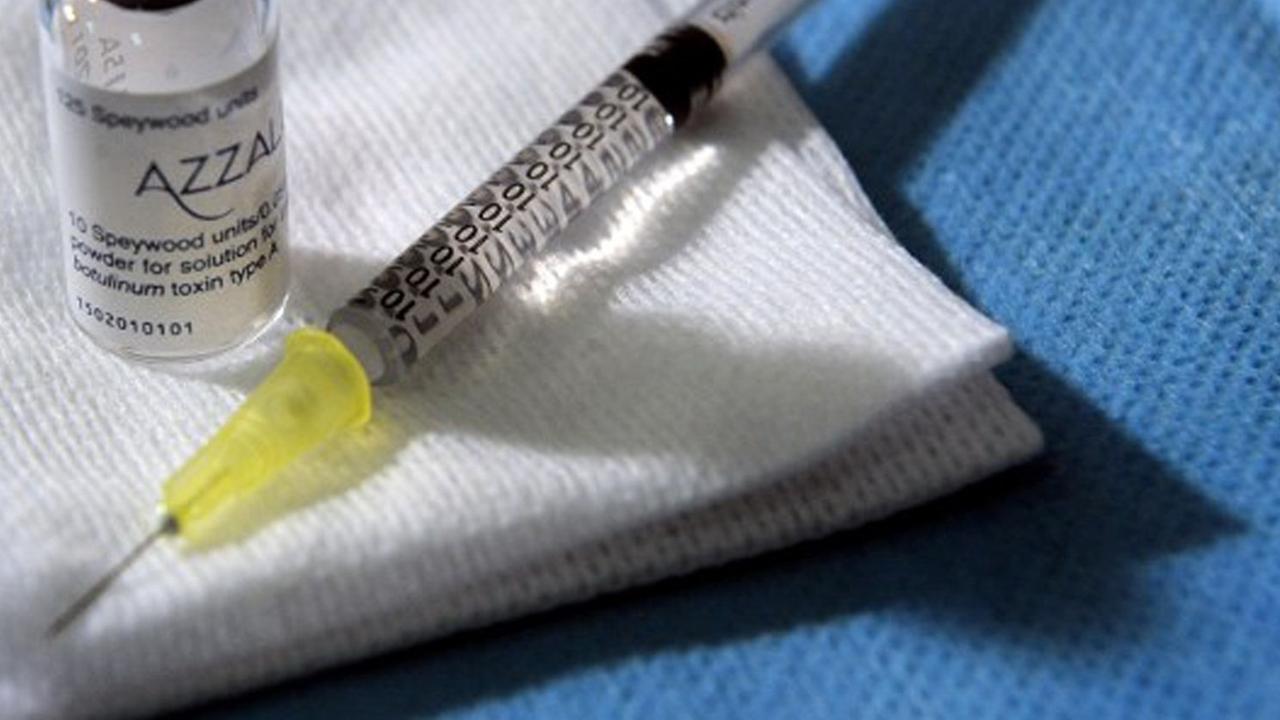 Auf einem blauen Tuch liegen auf weißen Tüchern eine Botox-Ampulle und eine Spritze parat.