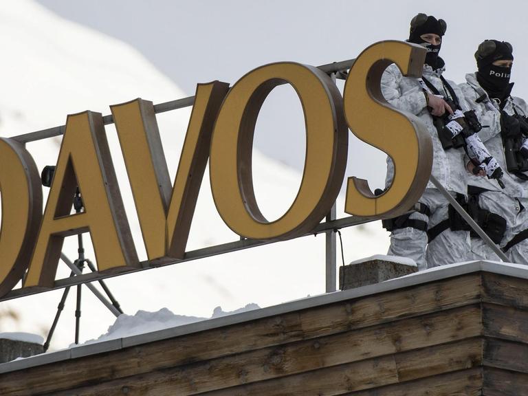 Vermummte Beamte der Schweizer Polizei in Wintermontur und Waffen stehen auf dem Dach des Kongresshotels in Davos.