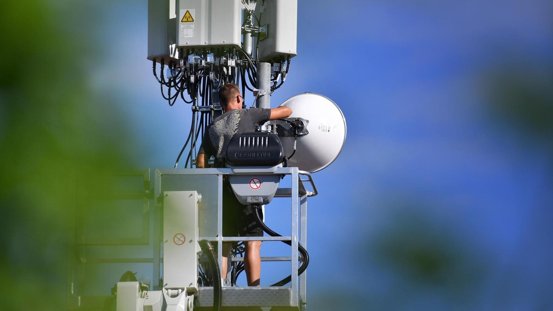 Ein Arbeiter steht auf einer Hebebühne und arbeitet an einem Antennenmast. Ein Arbeiter steht auf einer Hebebühne und arbeitet an einem Antennenmast.