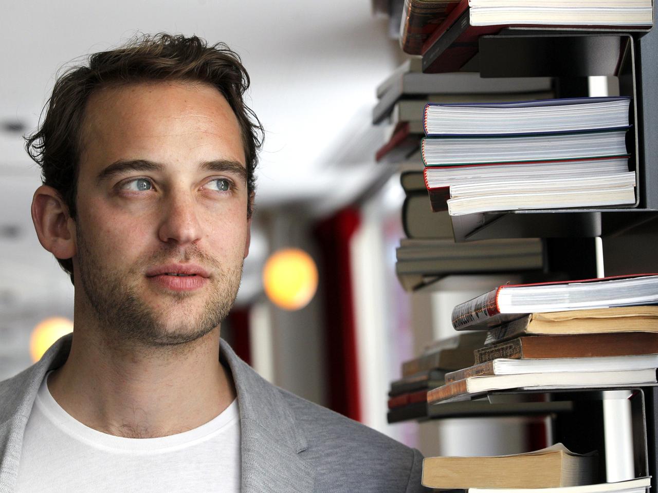 Portraitaufnahme des Autors Joël Dicker  neben einem Bücherstapel.