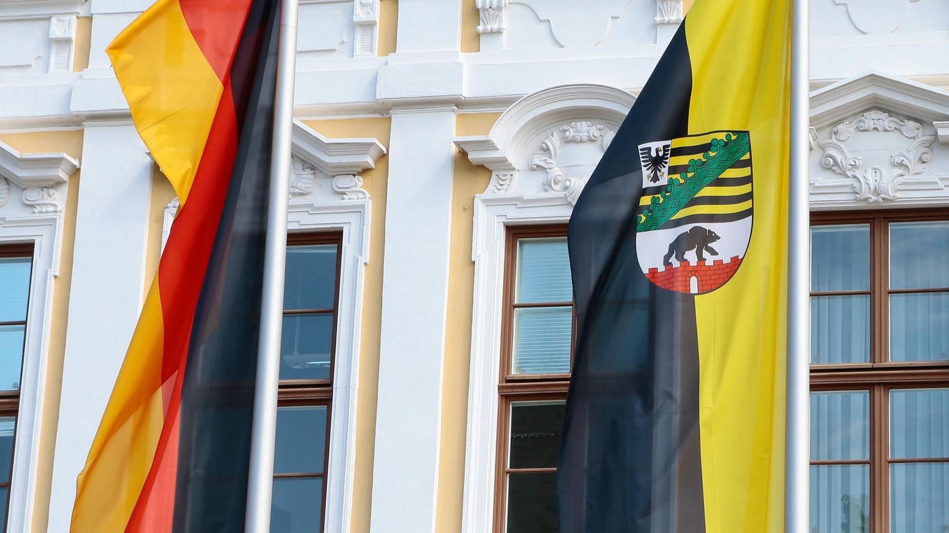 Deutschland- und Landesfahne von Sachsen-Anhalt vor der gelb-weißen Fassades des Landtags von Sachsen-Anhalt am Domplatz in Magdeburg.